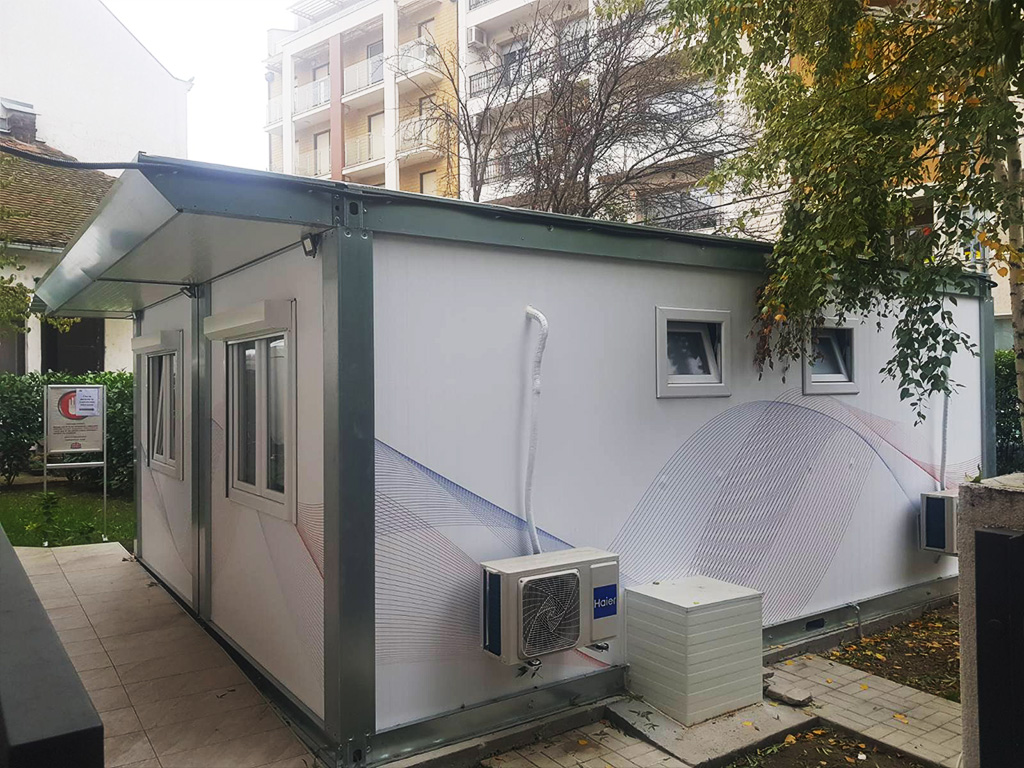 Weißer Container mit zwei Fenstern, kleiner Überdachung, Wandklimaanlage und externem Abwasserreservoir