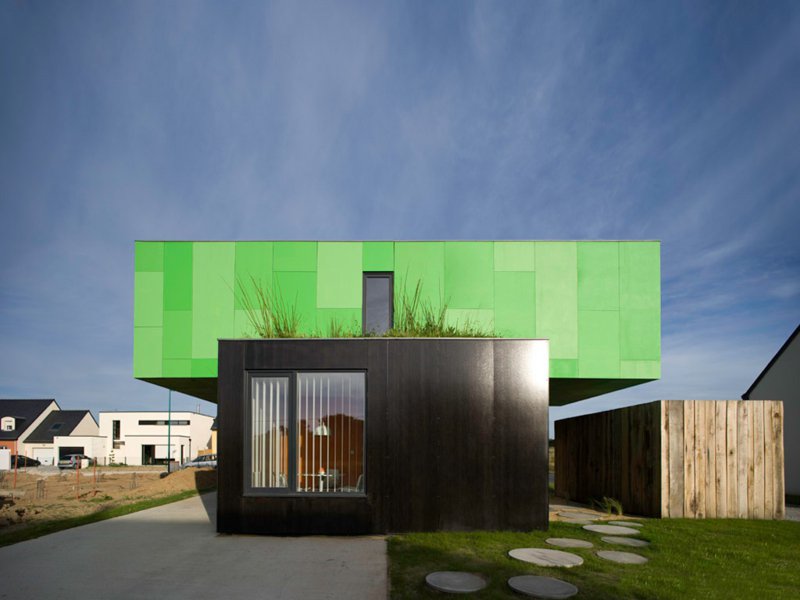 Modernes Wohnhaus aus Containern mit grünem Obergeschoss und schwarzem Erdgeschoss unter klarem Himmel.